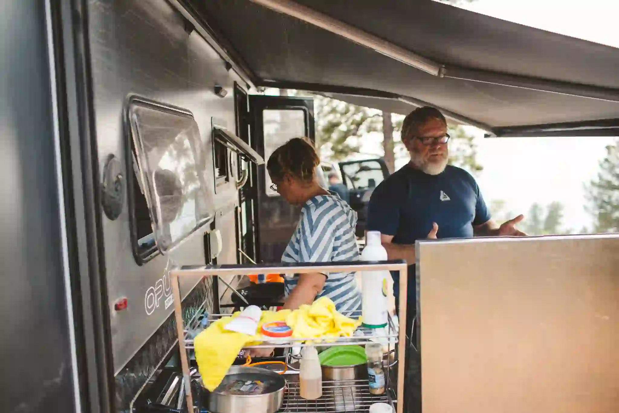 Two OPUS owners at the slide-out outdoor kitchen under the awning of their camper