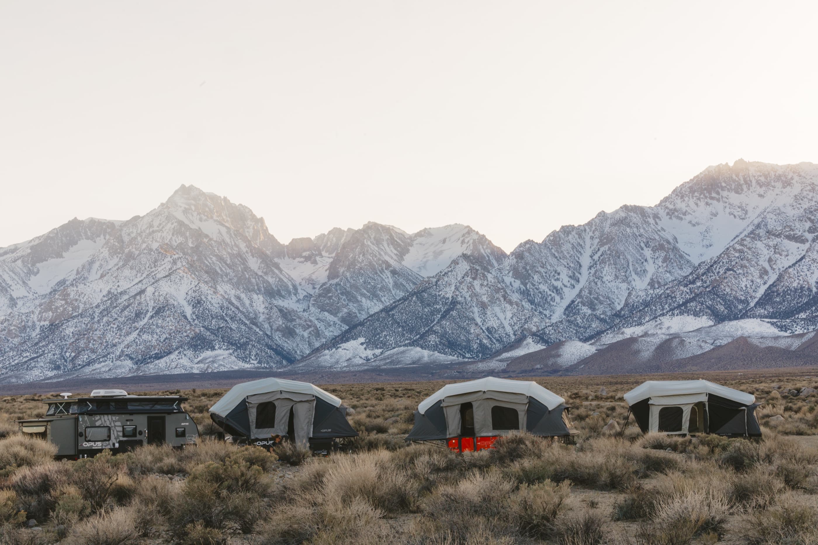 A row of OPUS campers set up below the snow-capped Sierra Nevada