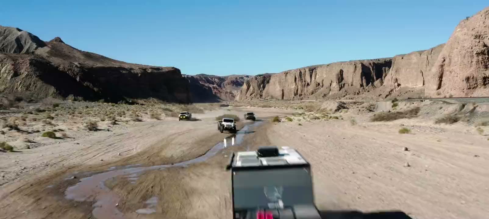 A convoy of Jeeps towing OPUS campers up a desert wash between canyon walls